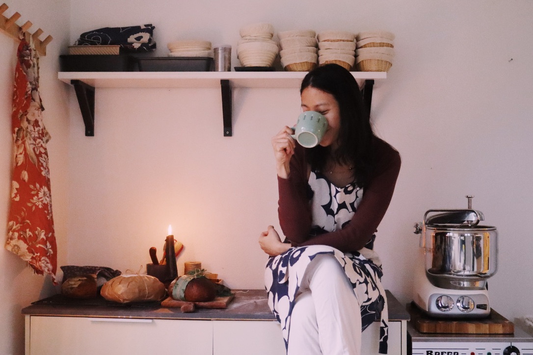 Zinnie sipping from a mug in a styled kitchen corner with bread and a candle